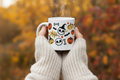 Fall Halloween 11oz Ceramic Mug held in cozy hands with knit sweater and warm fall foliage background